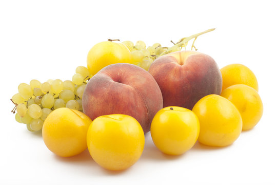 Two peaches, yellow plums and grapes branch on white