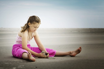Fototapeta na wymiar Mädchen sitzt am Strand und spielt