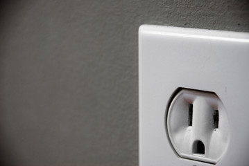 Close up of a white outlet on a gray wall.