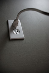 Long white cord plugged into a white outlet on a gray wall.