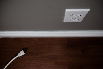 Unplugged cord on the floor beside a white electrical outlet.