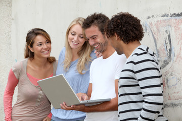 Group of friends standing against wall with laptop computer