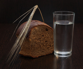 Bread, water  and wheat spike on wooden background.