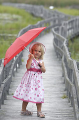 Little blond girl with red umbrella on boardwalk