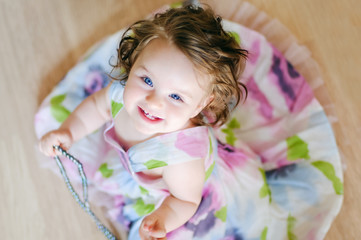 baby girl well-dressed sits on a floor and plays with chaplet