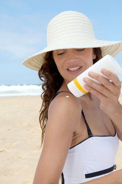 Beautiful woman at the beach putting sunscreen on her body