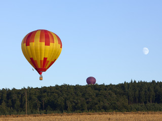 Naklejka premium Heißluftballons und Mond über Feld und Wald