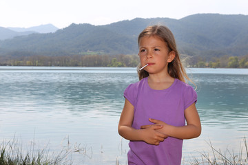 Girl standing by lake and sucking lollipop