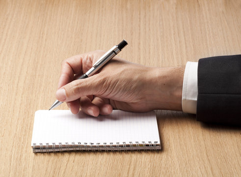 main &eacute;crivant au stylo-bille sur une feuille blanche