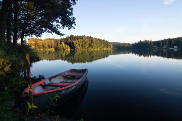 Obraz premium Evening summer countryside with pond, boat, forest and blue sky