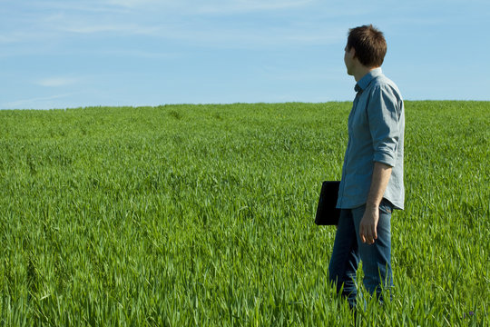 young man standing with a laptop in the green field
