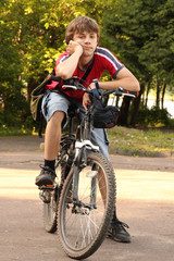 Fototapeta na wymiar Youth sits on bicycle in park and looks