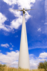 Fototapeta na wymiar Windmill in a field against a blue sky and clouds, alternative e