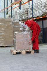 worker wrapping box on wooden pallet in warehouse