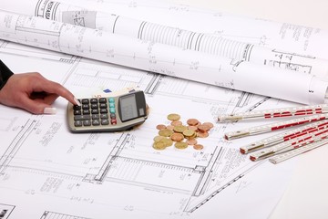 hand with house construction plan, calculator, coins