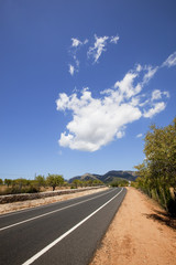 Fototapeta na wymiar Highway across non-urban landscape with blue sky and mountains