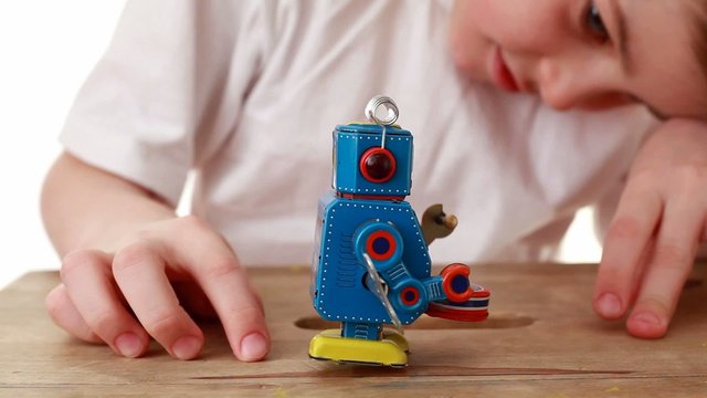 boy is watching going forward robot and tries to push him