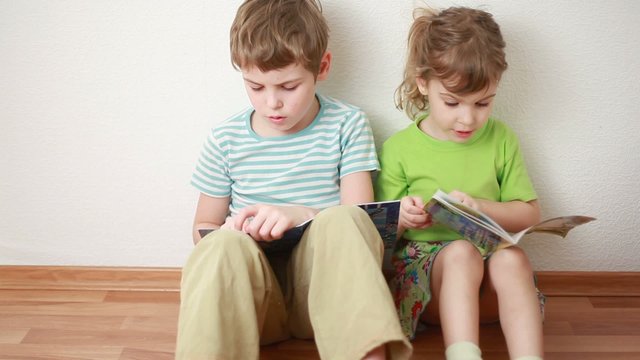 boy and girl sit leaning against wall and read books