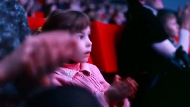 girl sits in auditorium of circus, watches show and claps