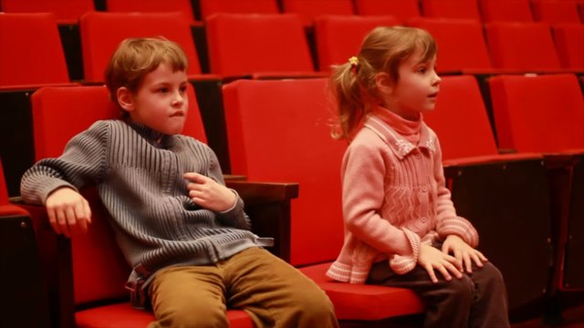 girl and boy sits in empty auditorium of circus and watches show
