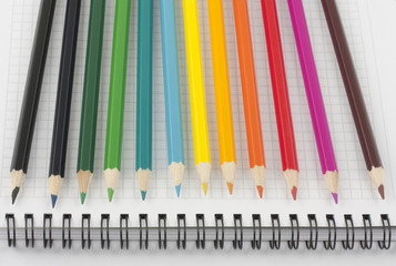 Multicolored pencils on opened spiral notebook