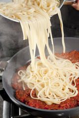Linguini being decantered onto tomato pesto.
