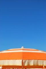 Orange striped beach umbrella on blue sky, Rimini, Italy