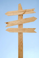Blank wooden direction signpost against a blue sky
