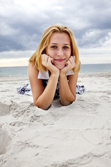 Beautiful blonde girl lying on sand at the beach in rainy day.