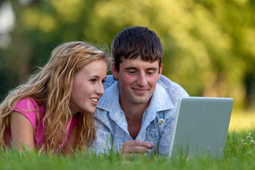 A couple relaxing in the park with a laptop