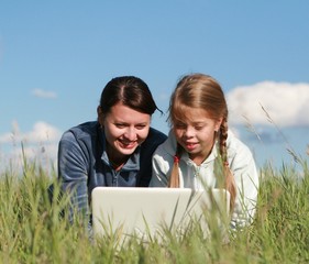 Two girls playing laptop on grass