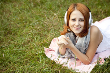 Young fashion girl with headphone lying at green grass