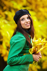 Fashion woman in autumn park holding yellow leaf