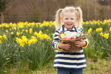Fototapeta premium Young Girl Holding Basket Of Decorated Eggs In Daffodil Field