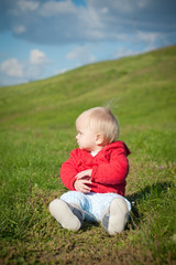 adorable baby sitting on green grass road within red jacket with