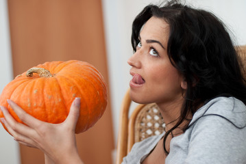 Attractive girl with dark hair holding pumpkins and licking