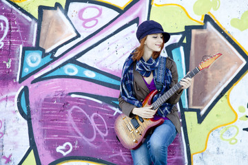 Obraz na płótnie Canvas Closeup portrait of a happy young girl with guitar and graffiti