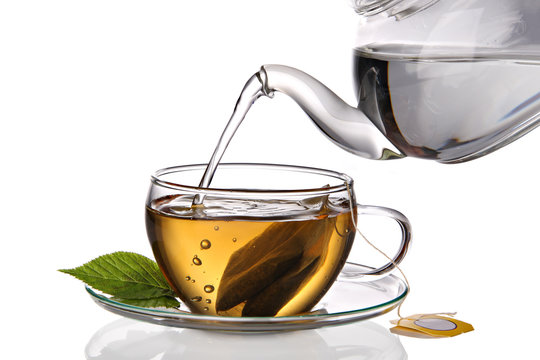 Water being poured into glass tea cup with teabag