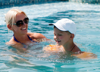 Smiling beautiful woman and little boy bathes in pool