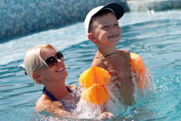 Smiling beautiful woman and little boy bathes in pool