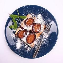 Piece of Plum Pie covered with powder sugar on a blue plate