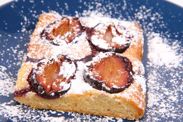 Piece of Plum Pie covered with powder sugar on a blue plate
