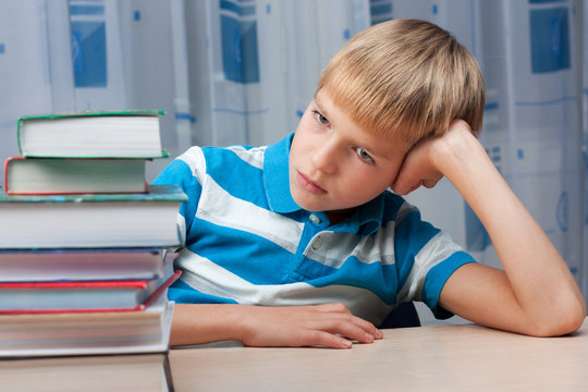 Sad boy at the table with a stack of books