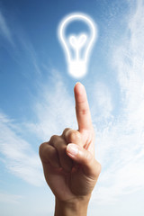 light bulb glowing on finger over blue sky