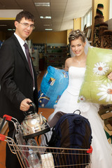 Smiling bride and groom with push cart with goods in store
