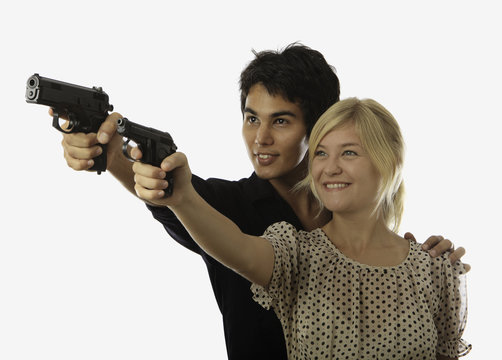 asian man teaches a young woman how to aim a pistol