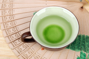 a cup of tea with chinese fan on bamboo tray