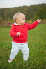 young cheerful baby stay on the grass in park with hand up