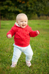 young cheerful baby running on the grass in park