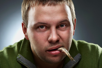 Studio fun closeup portrait of hungry man with fish in mouth